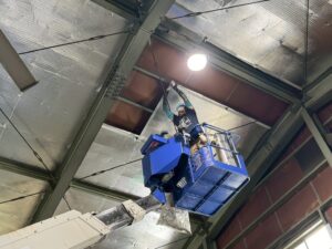 株式会社シンテック様工場内で高所作業車を使用し、屋根下にサーモバリアSを施工している作業風景。