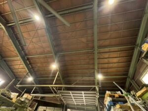 高所作業車を使用した施工前確認。株式会社シンテック様工場内で屋根下の施工範囲を確認している様子。